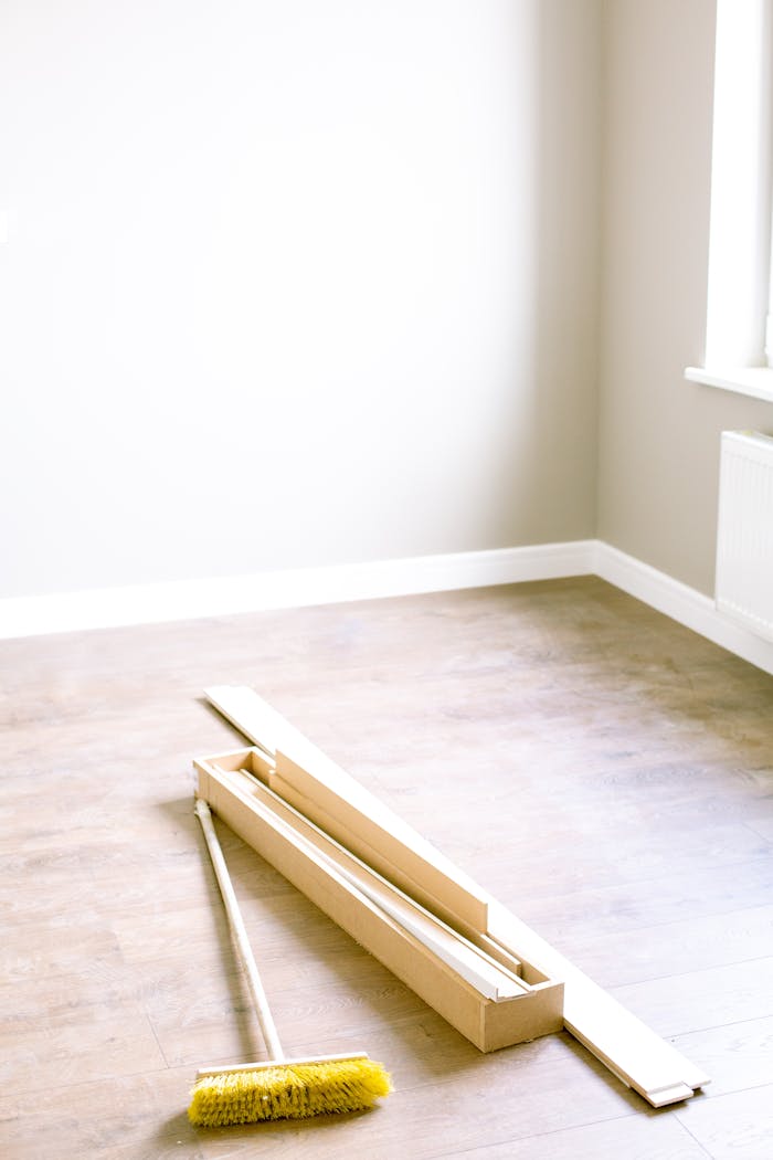 An empty room with wood planks and a broom, ready for renovation.